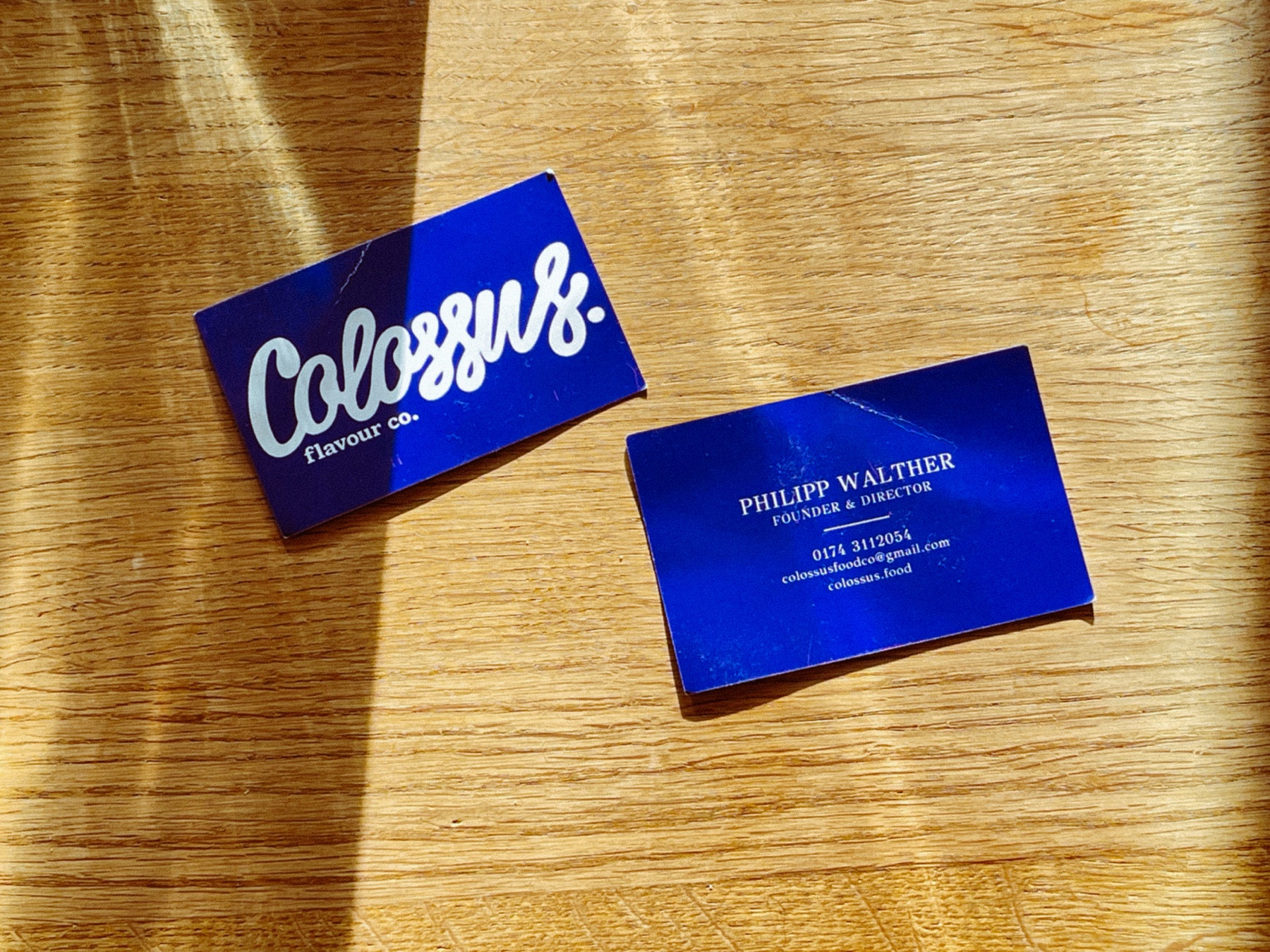 Colossus flavour co. business cards on a sunlit wooden table